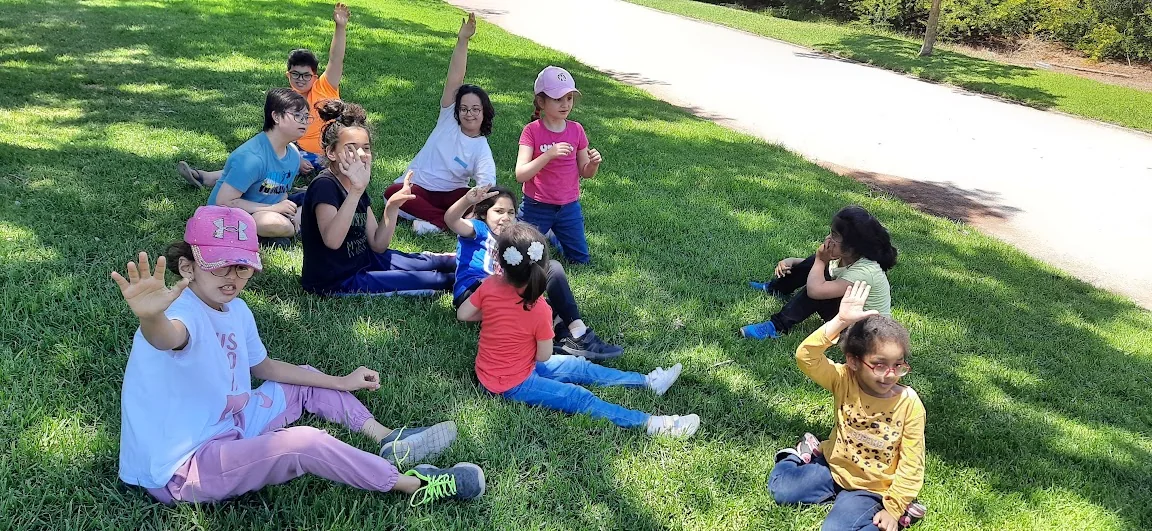 Enfants assis dans l’herbe d’un jardin, mains levées